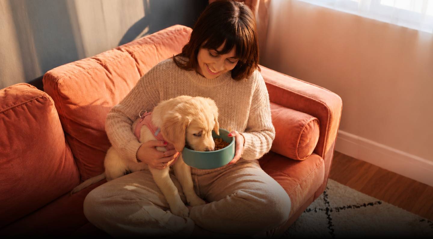 A woman feeding her golden retriever puppy from a Snuggles bowl
